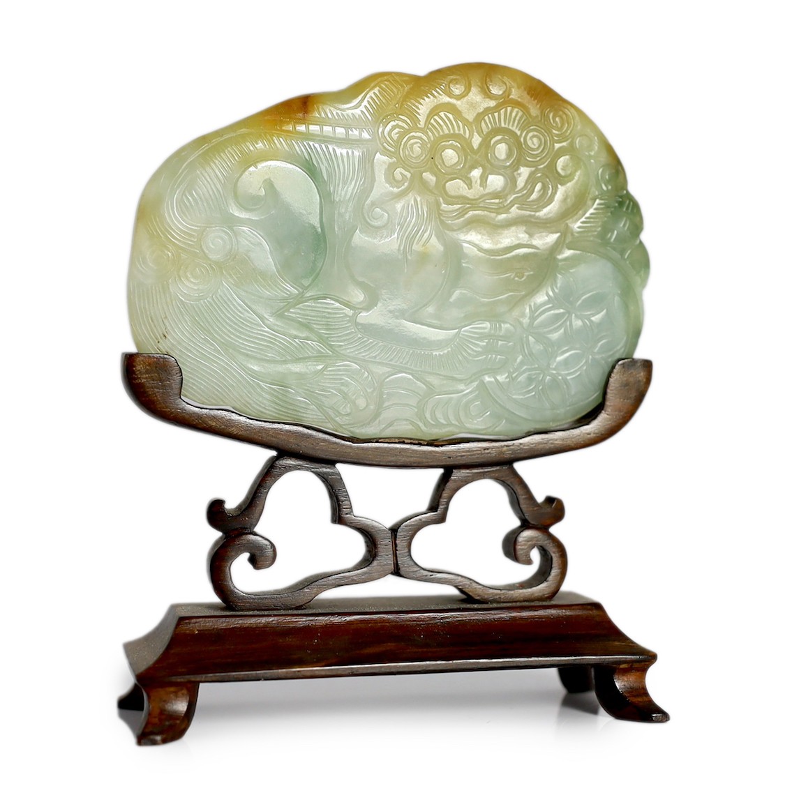 A Chinese three colour jade 'Buddhist lion' belt buckle, 19th century, 8cm across, wood stand